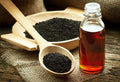 Black sesame oil in glass bottle with wooden spoon and dark seeds