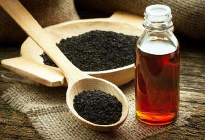 Black sesame oil in glass bottle with wooden spoon and dark seeds
