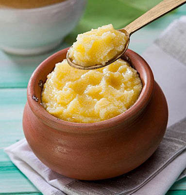 Melted ghee in terracotta bowl with wooden spoon, thick golden texture