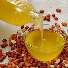 Groundnut oil being poured into glass bowl with peanuts scattered