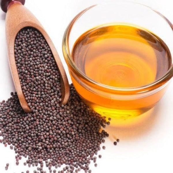 Mustard oil in a clear glass cup with visible seeds, golden yellow liquid