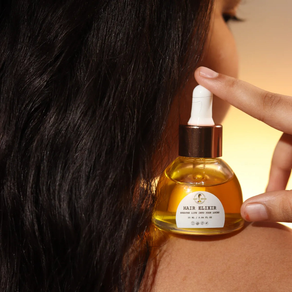 Hair elixir bottle with white pump held near dark hair, 30 ml.