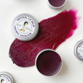 Natural lip balm tin with beetroot-colored balm swatch, round metal container.
