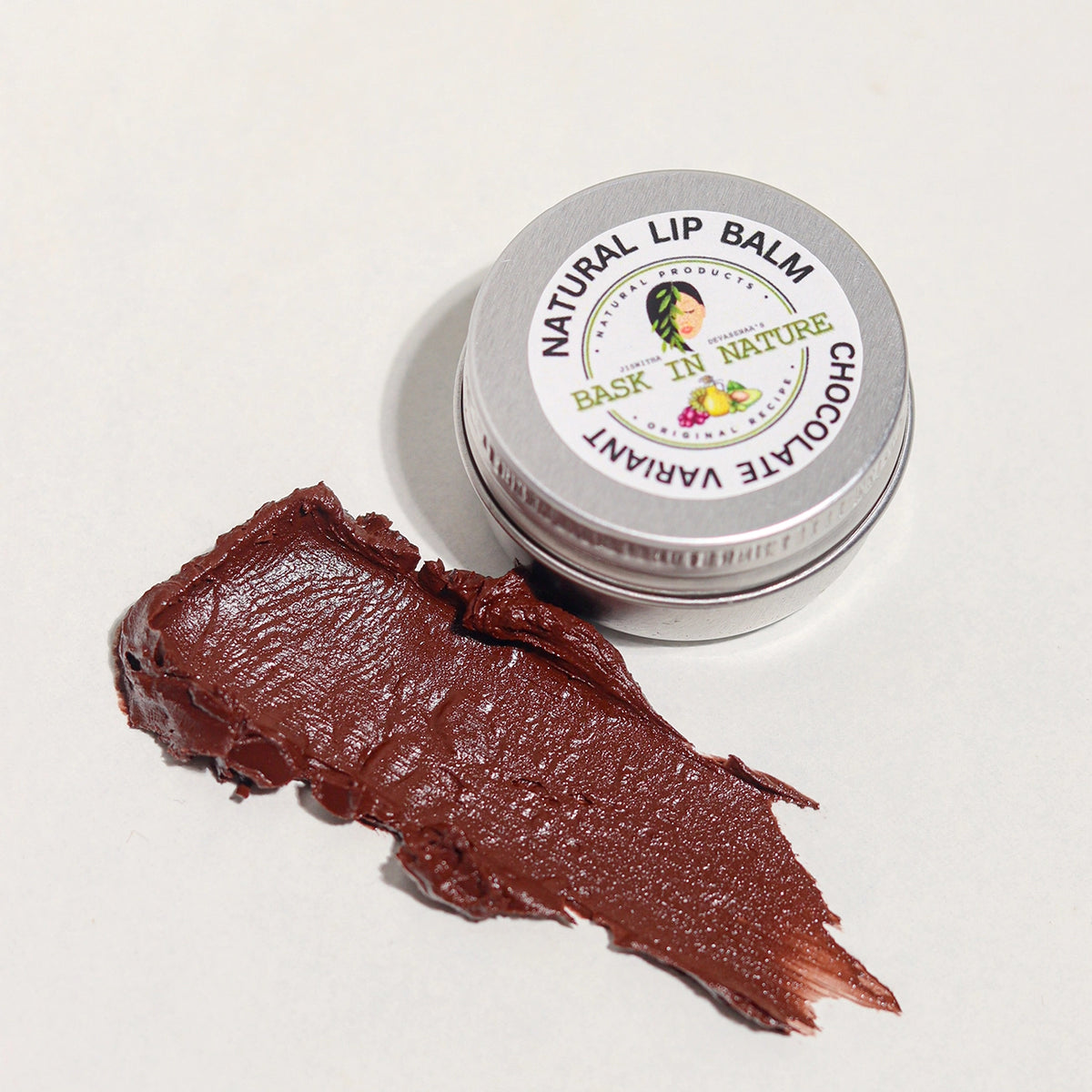 Chocolate lip balm tin with dark brown balm swatch on a light background