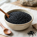 Kalonji seeds in a ceramic bowl with wooden spoons, dark black