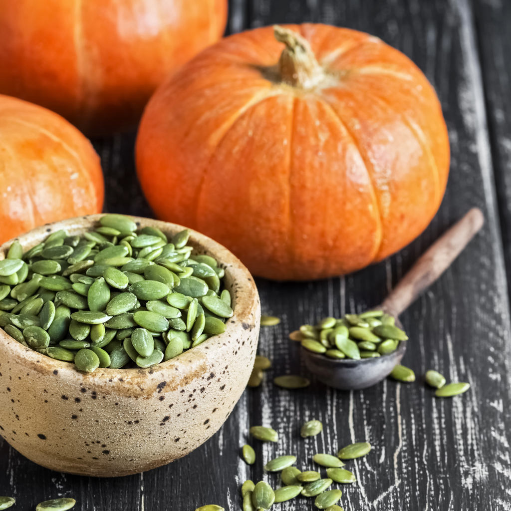 Green pumpkin seeds in speckled ceramic bowl with loose kernels
