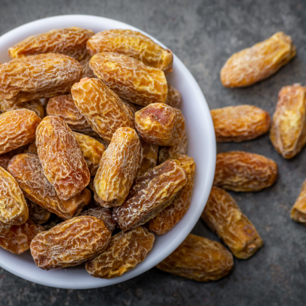 Bowl of yellow dried dates with more dates scattered on a dark surface