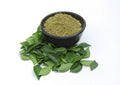 Curry leaf powder in a bowl with fresh green curry leaves on the side