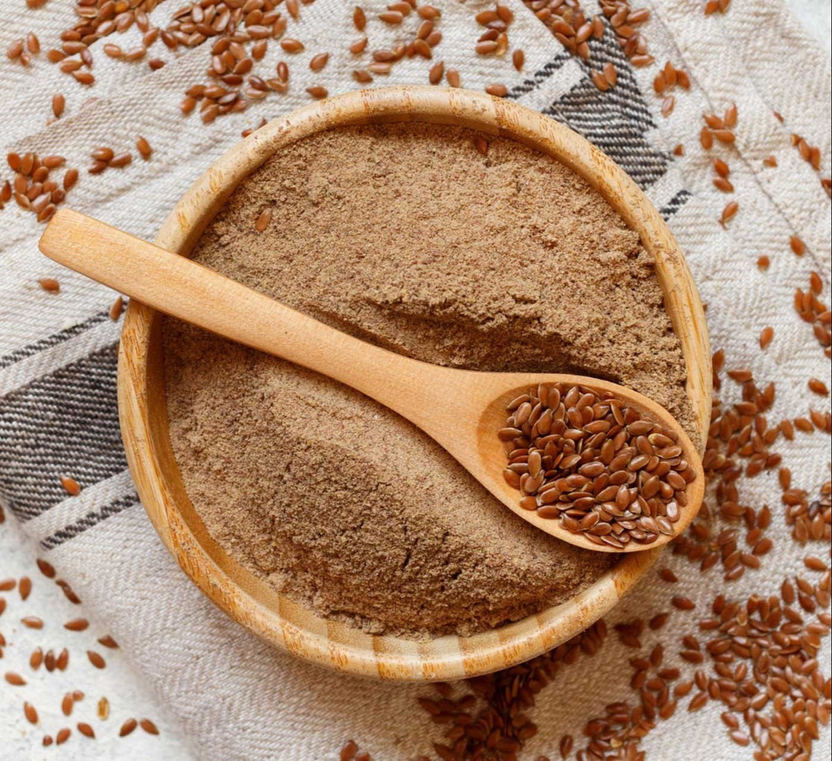 Ground flax seeds powder in wooden bowl with wooden spoon, light brown