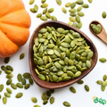 Green pumpkin seeds in a wooden bowl with scattered seeds around