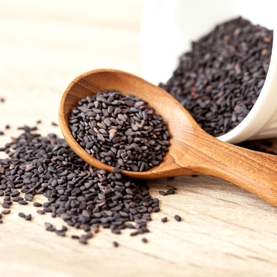 Black sesame seeds in wooden spoon, dark seeds scattered on wood