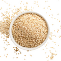 White sesame seeds in a white bowl, scattered around.