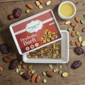 Dry fruits burfi in open tray with chopped nuts scattered, small bowl beside it.