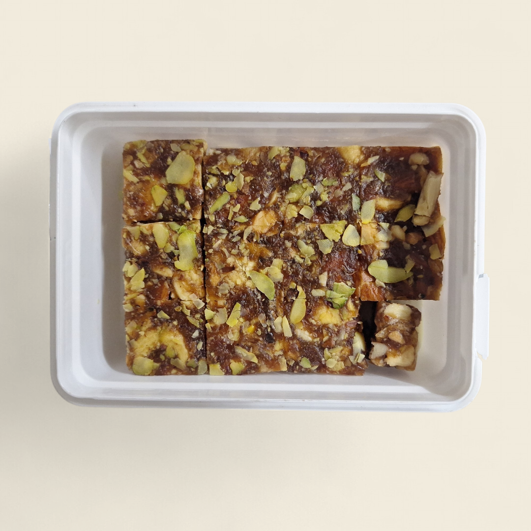 Dry fruits burfi pieces with mixed nuts in white tray, top view.